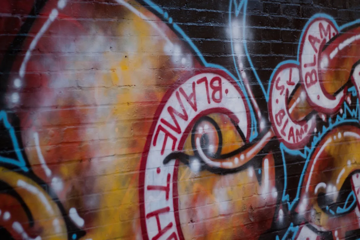 Graffiti in red and orange with the words Blame The lettered along a curling ribbon.