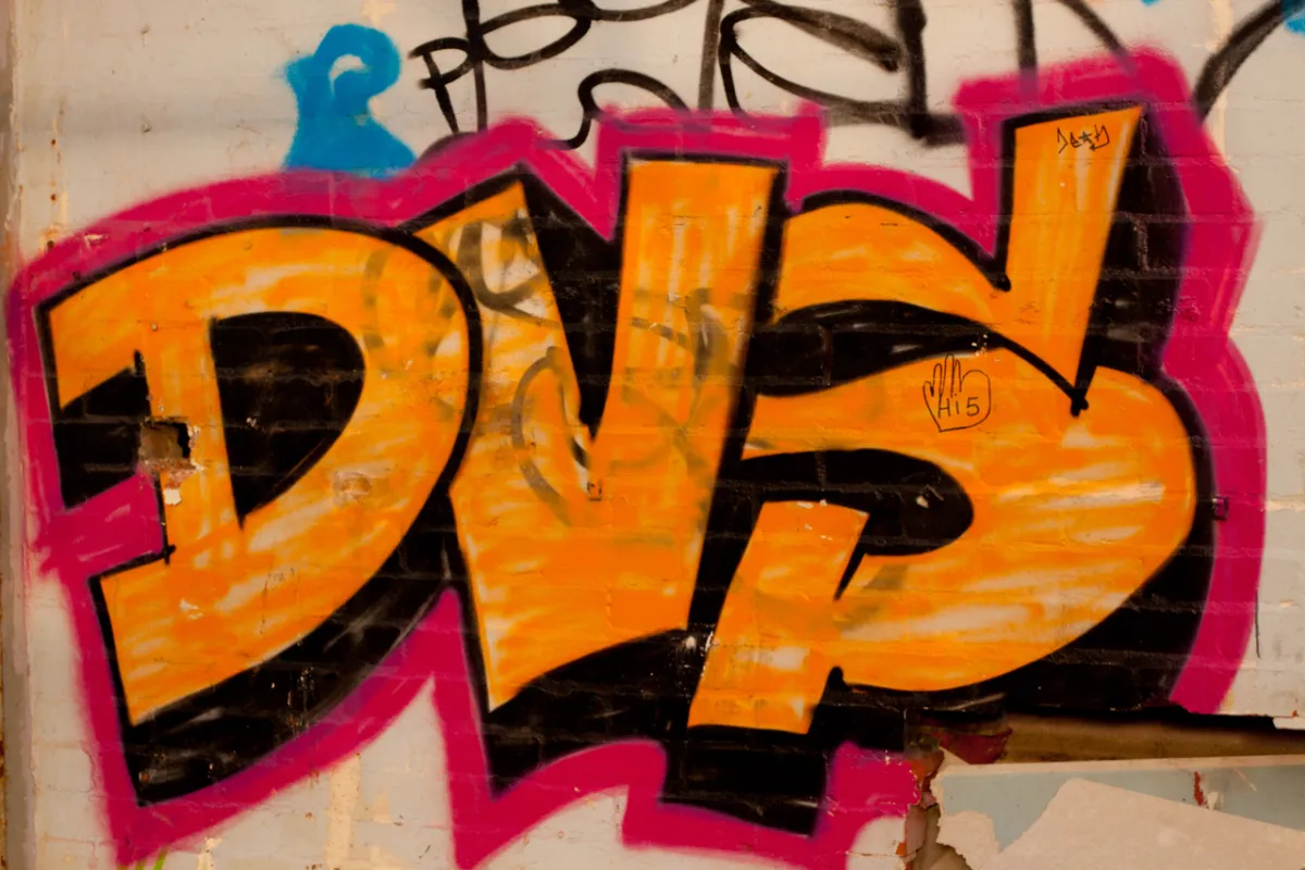 Large orange bubble-letter graffiti outlined in pink on a brick wall.