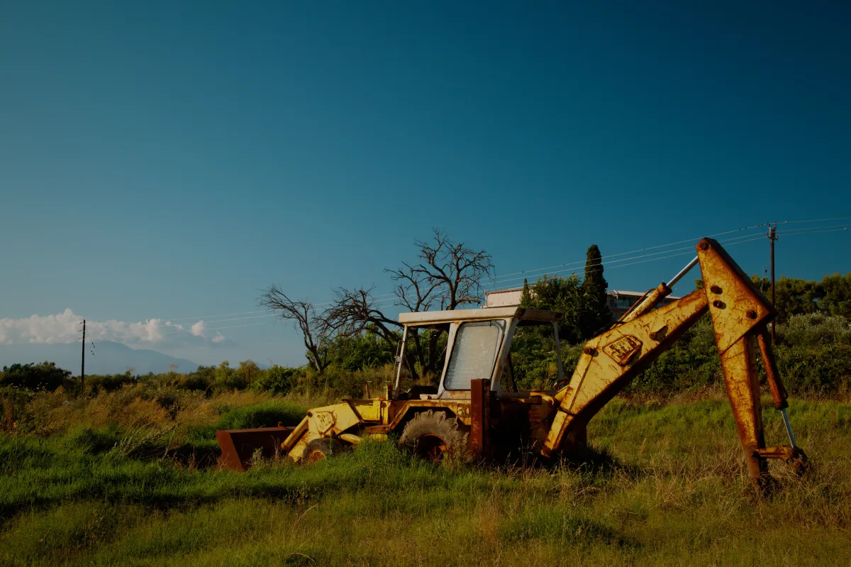 A rusting yellow JCB digger standing in long grass.