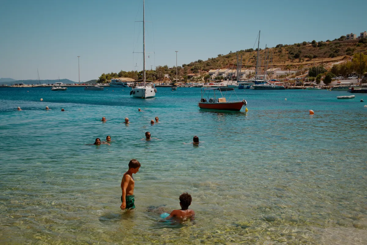 Children playing in clear shallow water, with boats moored further out.