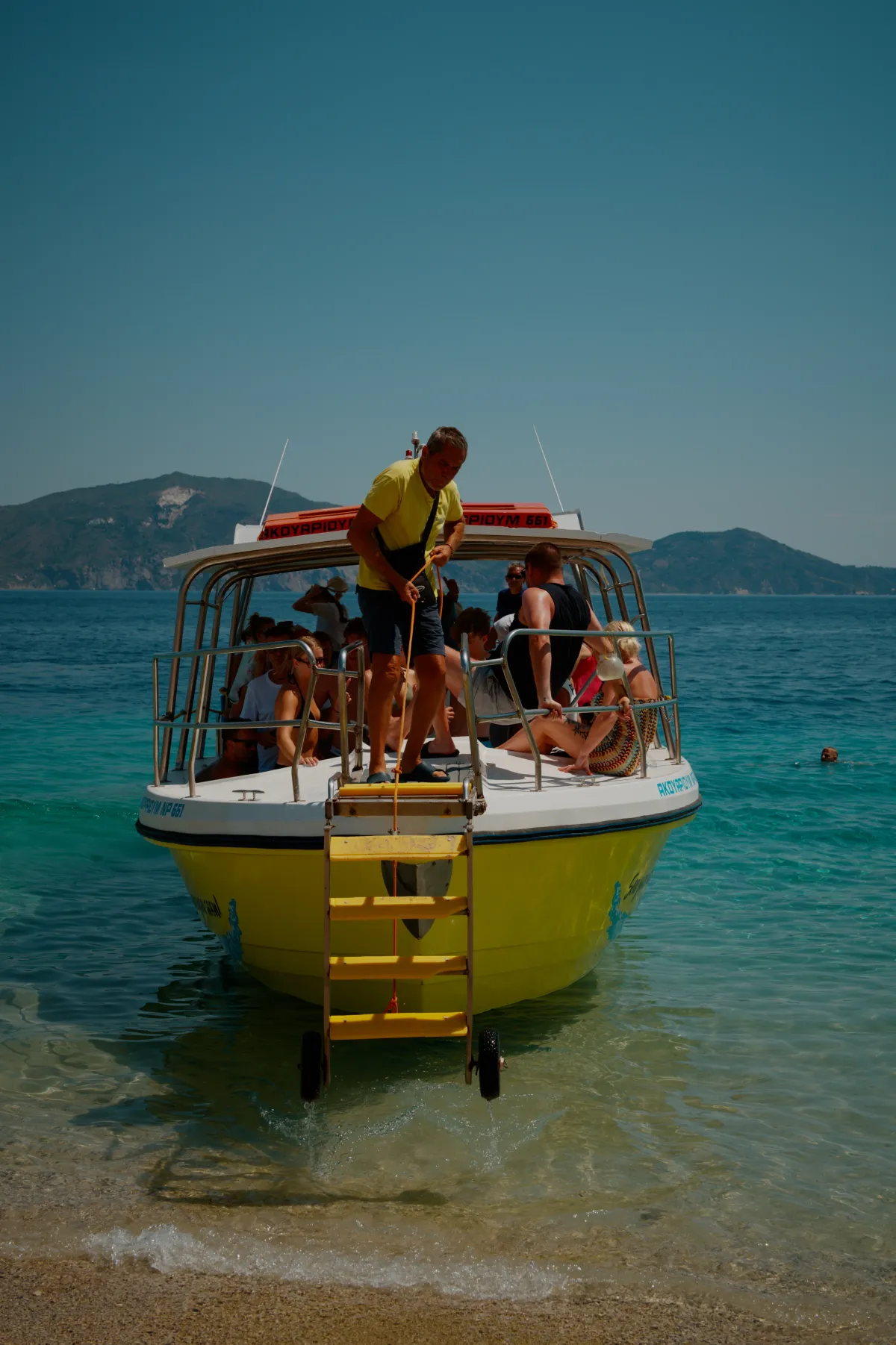A yellow excursion boat pulled up to a beach with passengers on board.