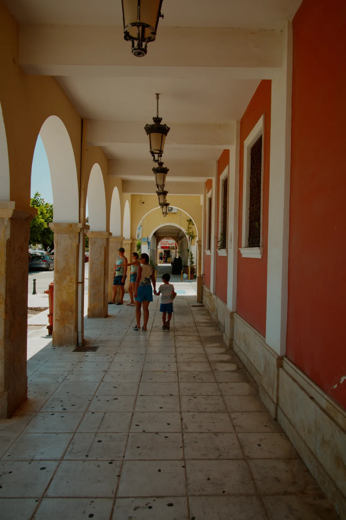 A colonnaded arcade with hanging lanterns, people walking through.
