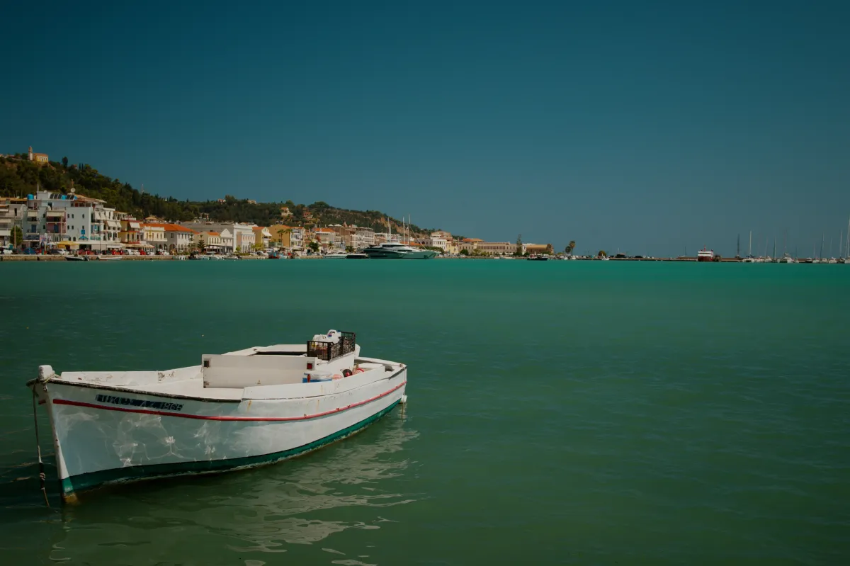 A small white boat on turquoise water, with the harbour town behind.
