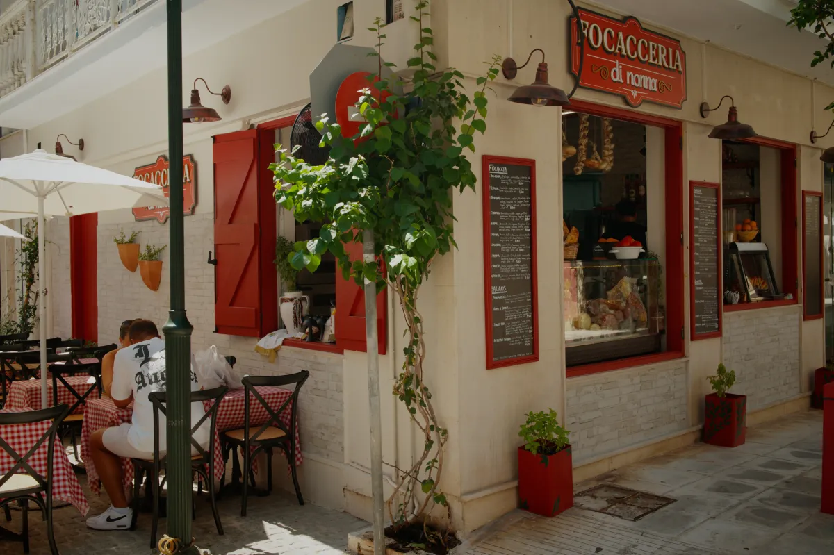 A focacceria with red shutters, and people sitting at tables outside.