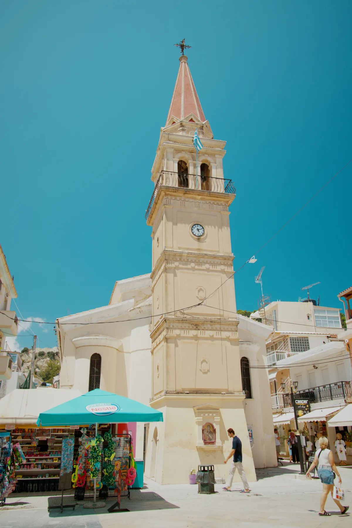 A stone church bell tower with a clock face, market stalls below.