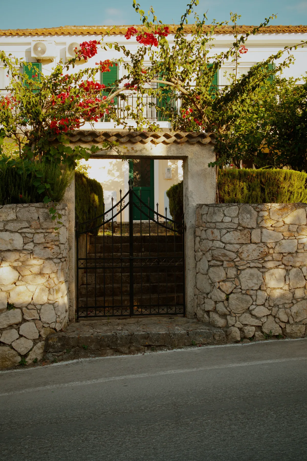 A wrought iron gate in a stone wall, with bougainvillea growing over the entrance.