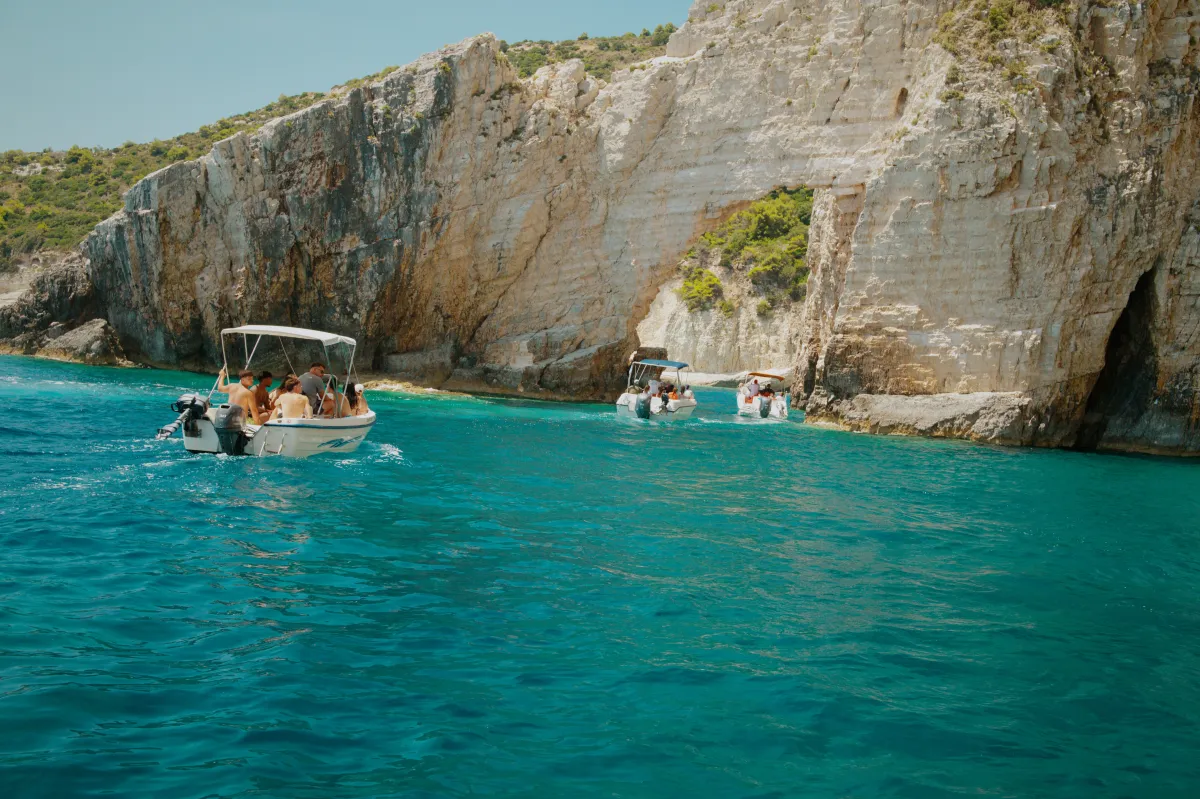 Small boats on turquoise water beneath white cliffs and a sea cave.