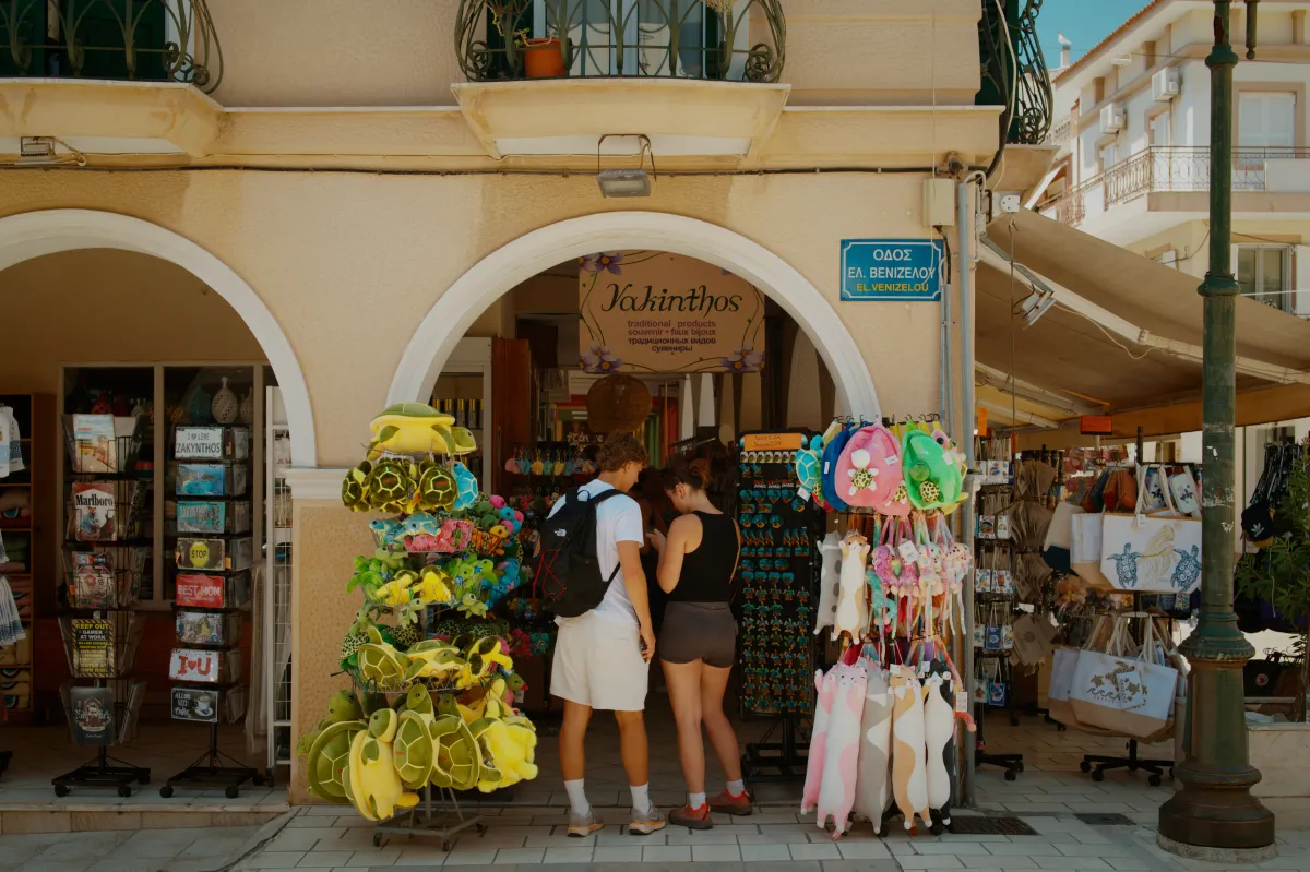 Two people looking at a souvenir shop under an archway, goods hung outside.