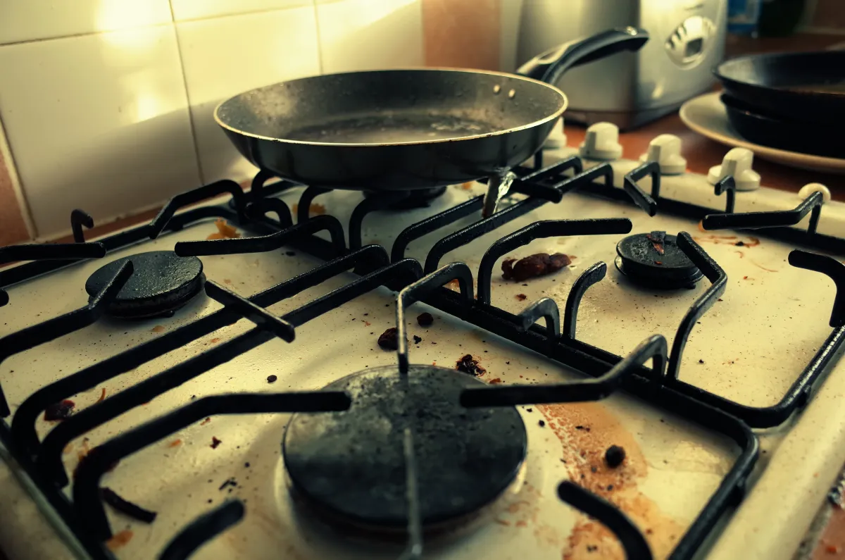 A dirty gas hob with a frying pan placed on one of the rings.